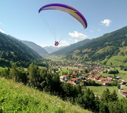 Paragleiter zieht seine Kreise über Gastein. Er ist gerade gestartet, im Tal der Ort Hofgastein, blauer Himmel mit vereinzelten weißen Wolken. 