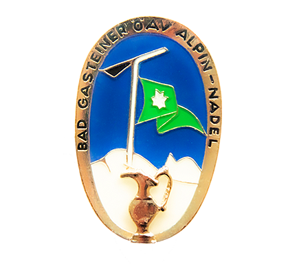 Die Bad Gasteiner Wandernadel, rund, mit blauem Himmel und im Wind whender Flagge. Im Vordergrund der berühmte Krug.