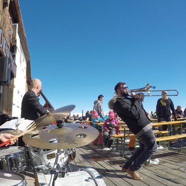Jazzmusiker auf der Terrasse einer Skihütte vor Publikum auf Bierbänken
